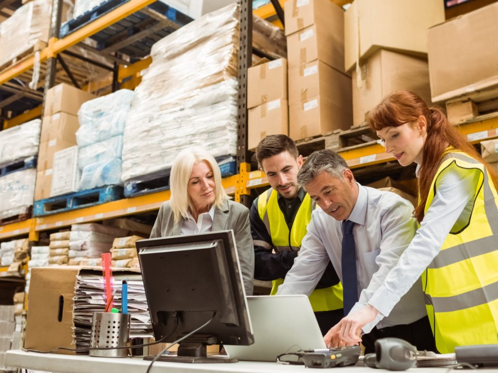 Warehouse managers and a worker reviewing receiving information together inside a large distribution facility